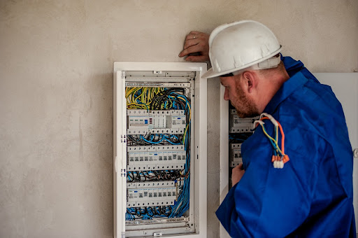 An electrician with a hard hat on investigating a breaker. 